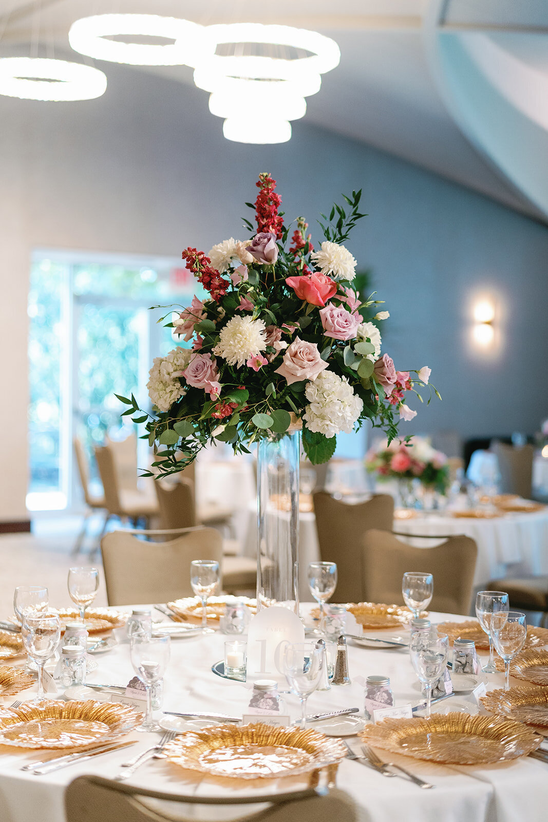 Elegant reception tables featuring tall candle-lined centerpieces, delicate floral arrangements by Always in Bloom, and soft gold accents.