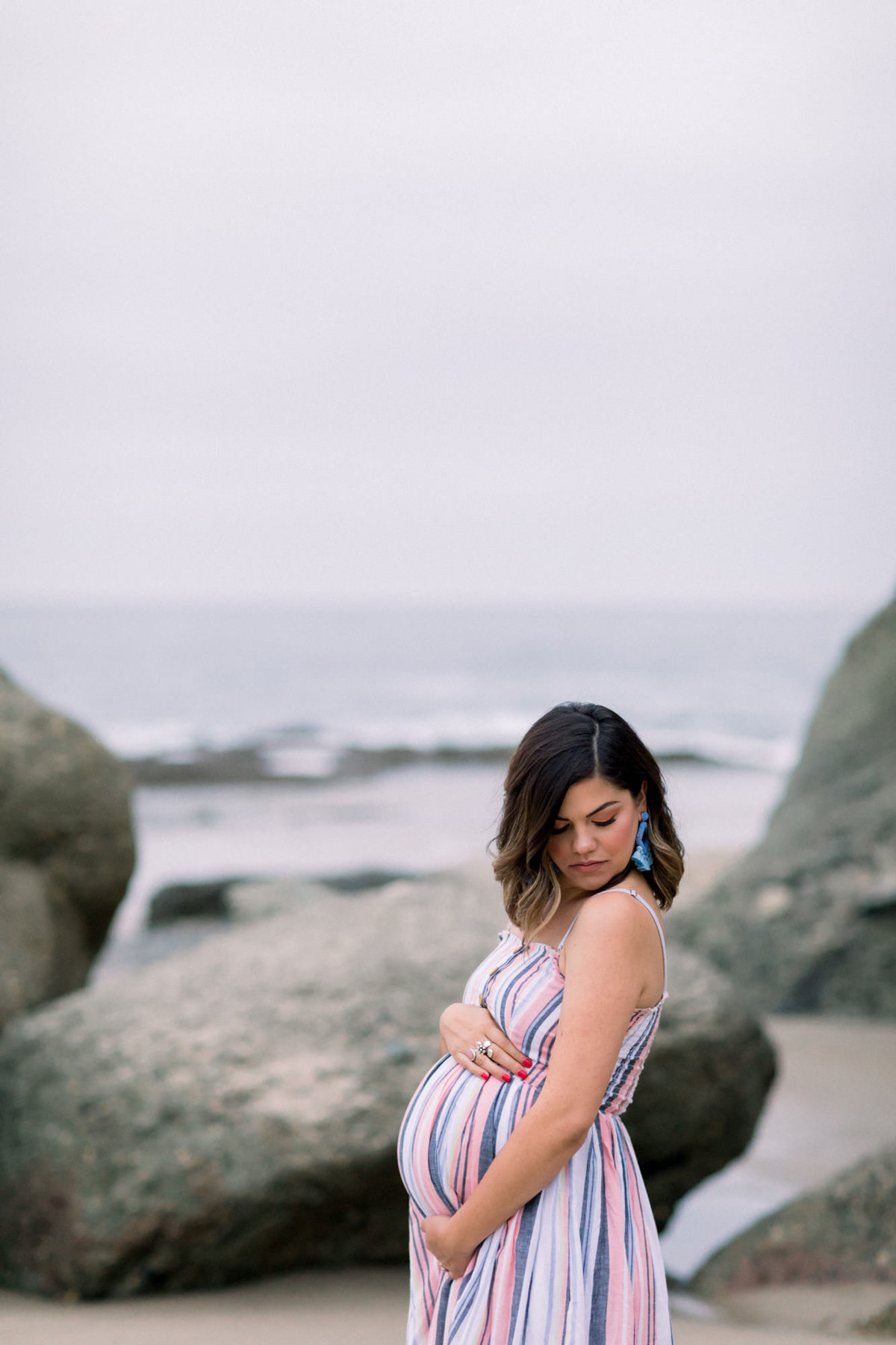 Young woman poses on the beach amongst the rocks for a maternity photography shoot