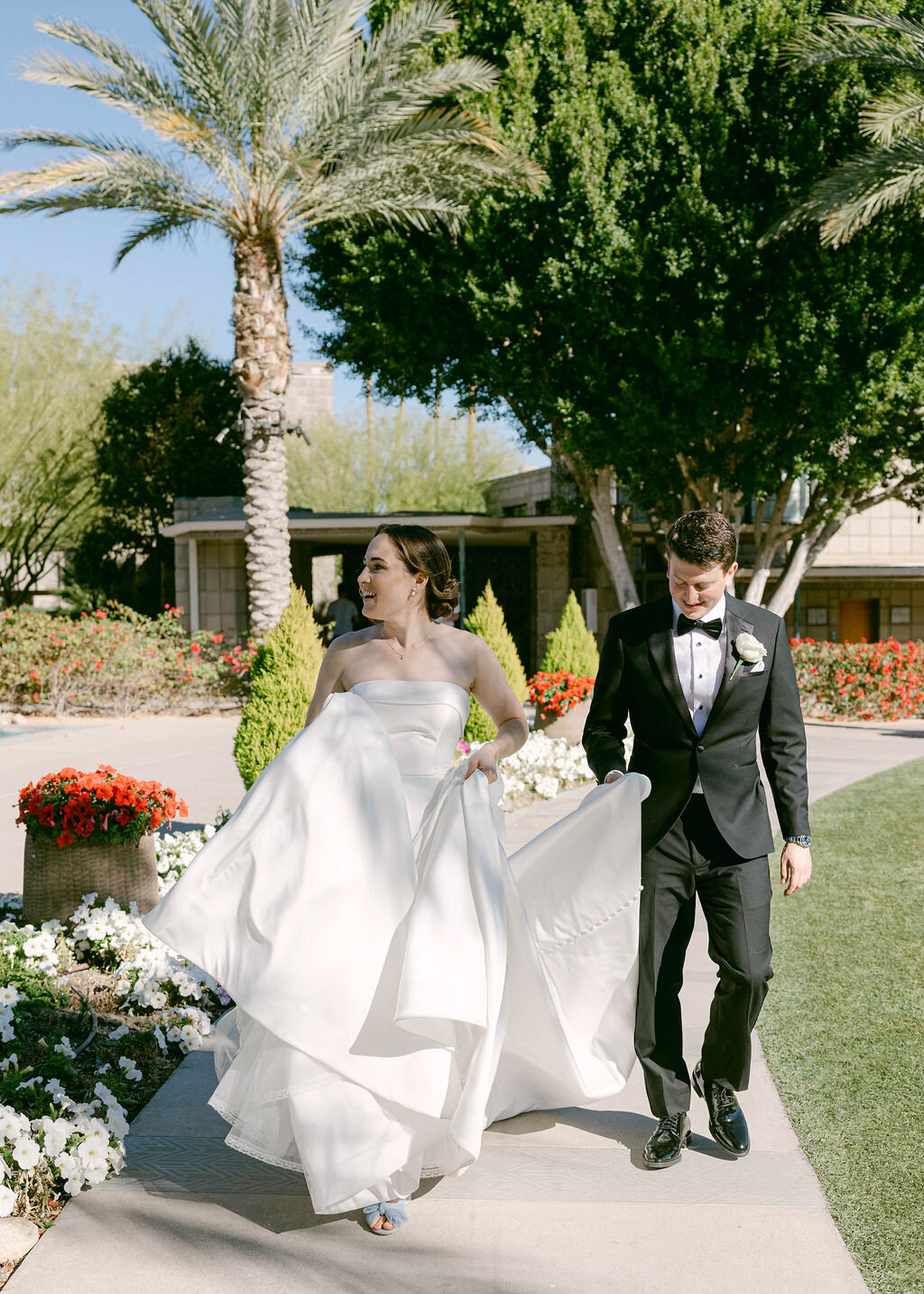 Joyful moment of bride and groom walking together at Arizona Biltmore wedding garden.