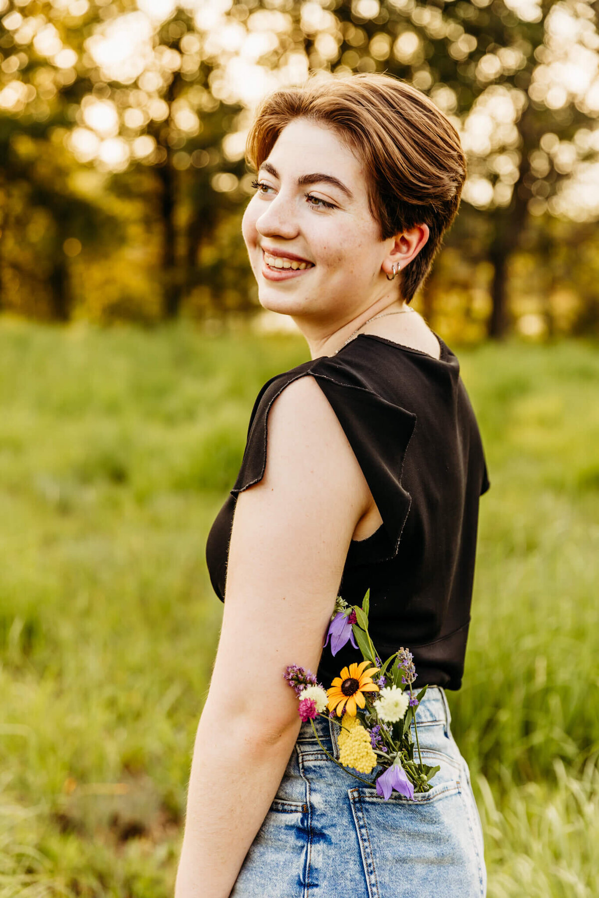 pretty teen girl with short brown hair glancing over shoulder with wildflowers in her back pocket by Ashley Kalbus