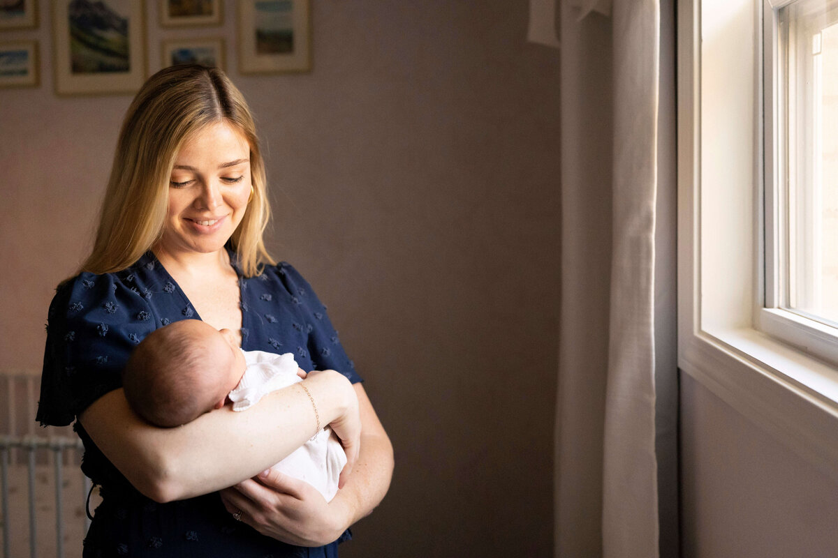 Mother standing by window and holding newborn duaghter in her arms