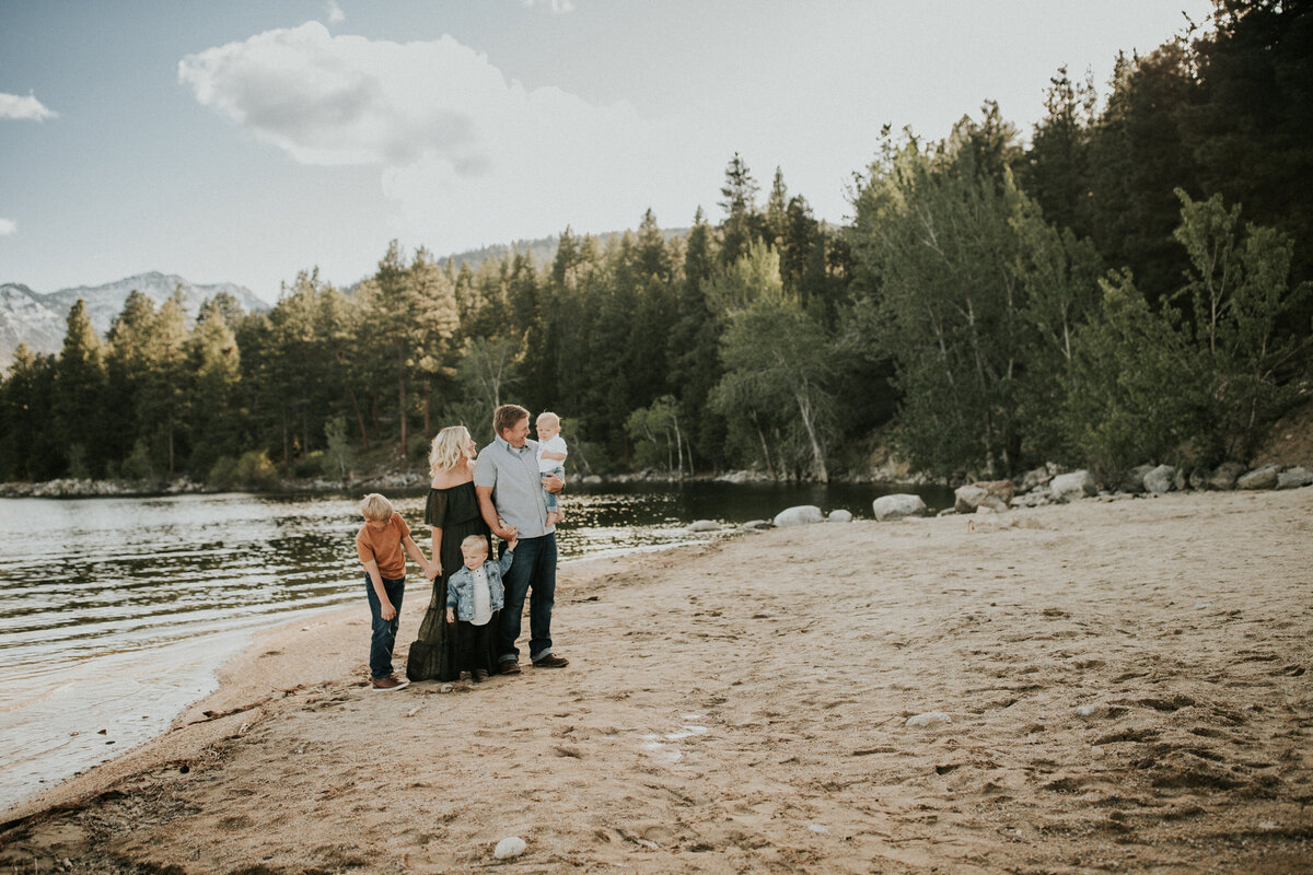 Family of five holds hands while looking at one another in front of a lake