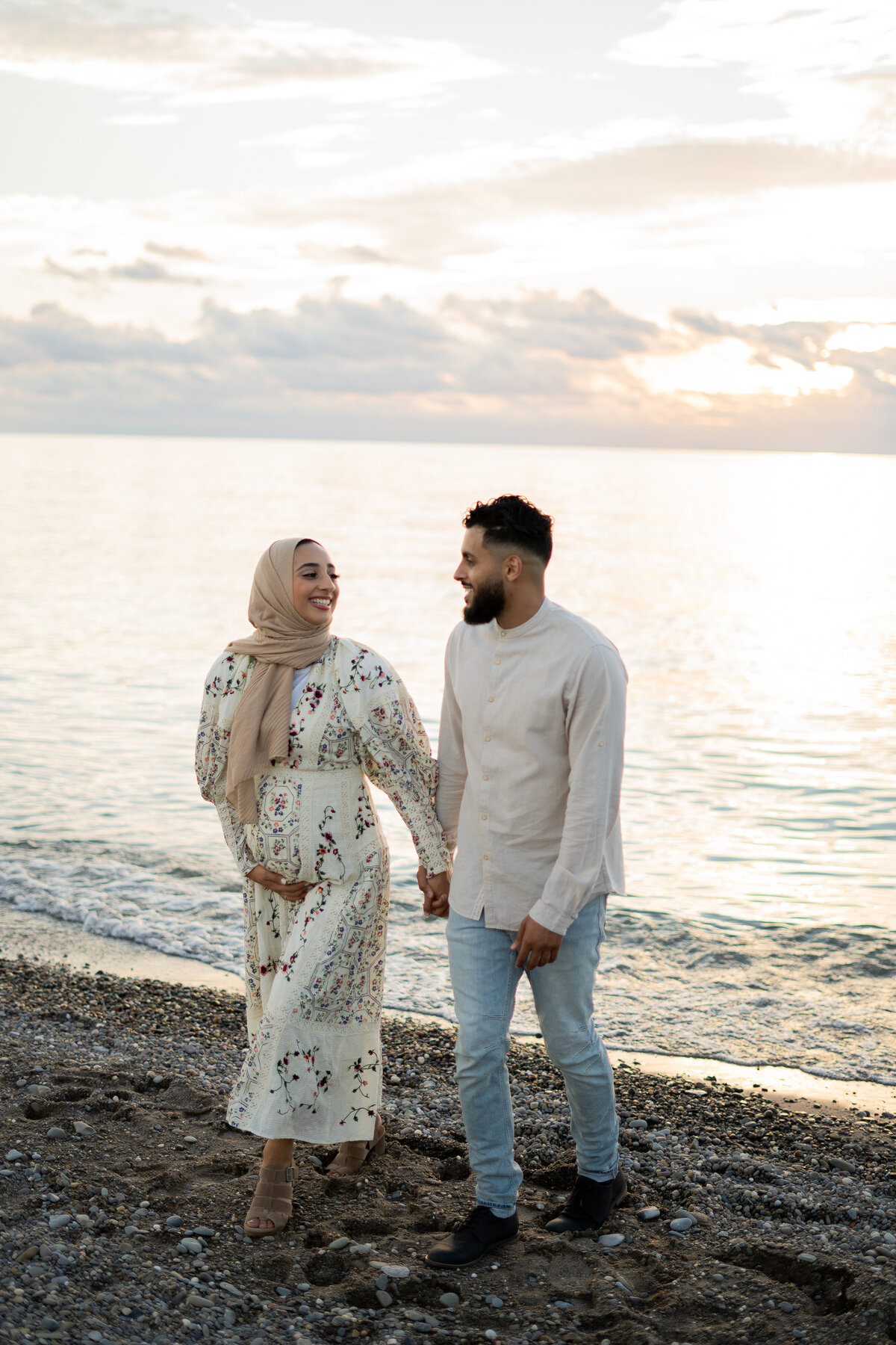 couple walking and laughing on the beach with soft golden hour light during maternity session in Cleveland