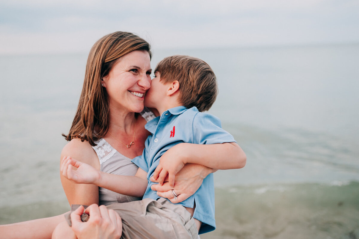 A mother holds her son next to the ocean while he whispers in her ear