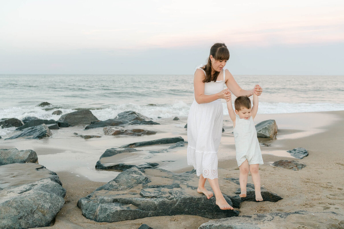 Mother holds son's hands on the rocky shoreline