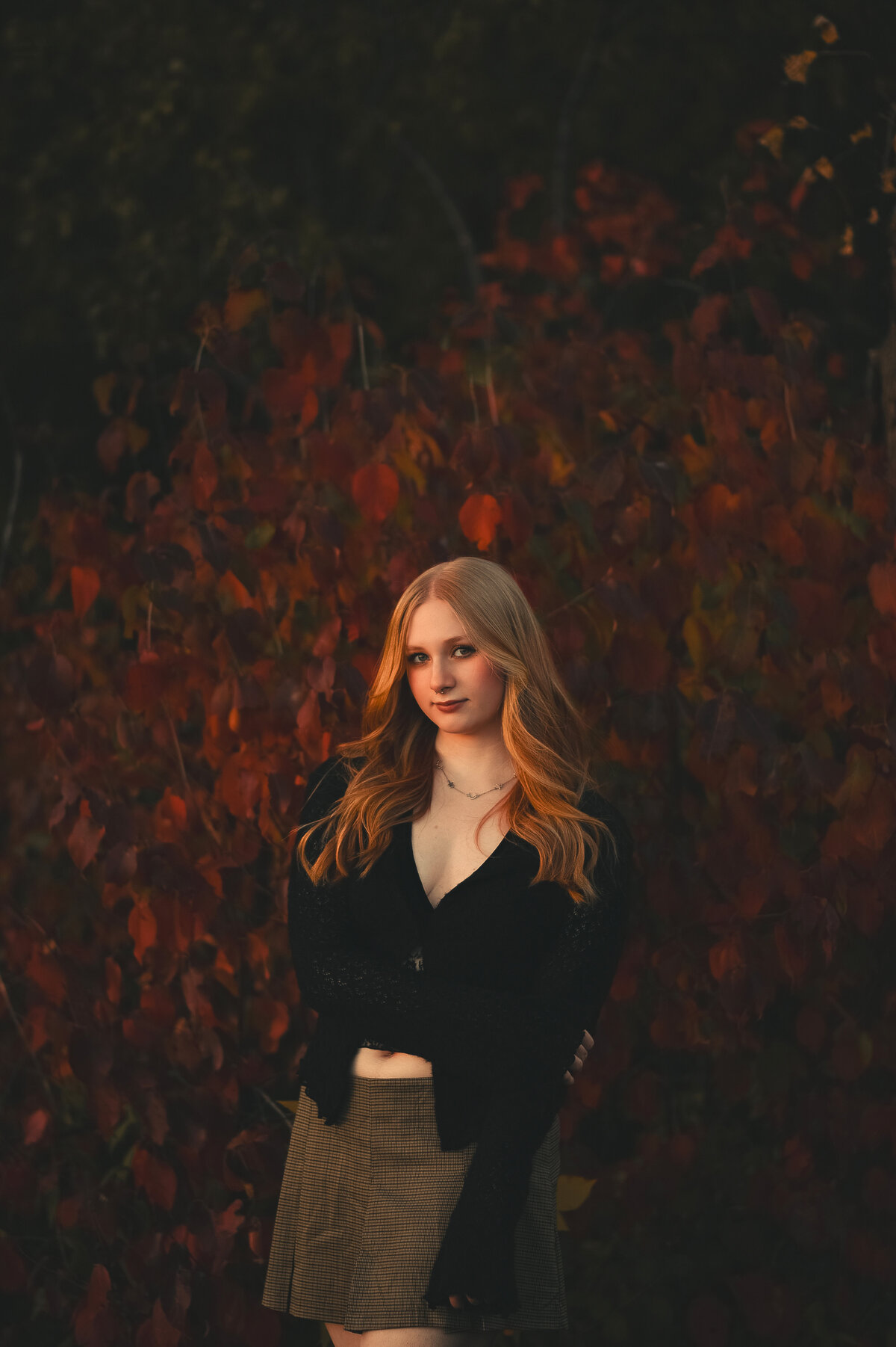 Photo by Shannon Kathleen Photography. Female high school senior standing against a bright red tree in soft golden light