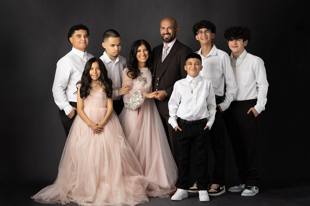 A joyful family, photographed by a Dallas family photographer, standing together in elegant attire against a neutral background, showcasing love and connection.