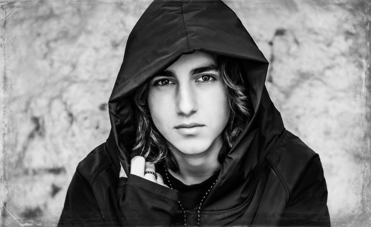 Male musician portrait Dominique Ilie black and white wearing hoodie hand holding collar against stone wall backdrop