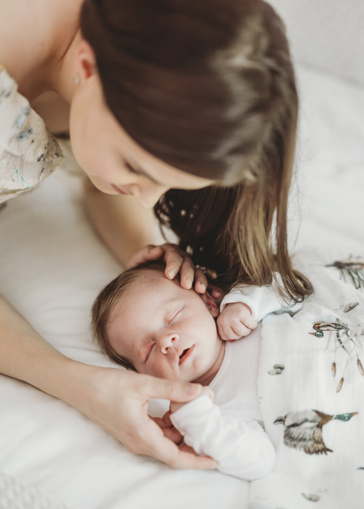 Close-up of a mother smiling down at her sleeping newborn in a floral onesie during a peaceful Kansas City newborn photo session.