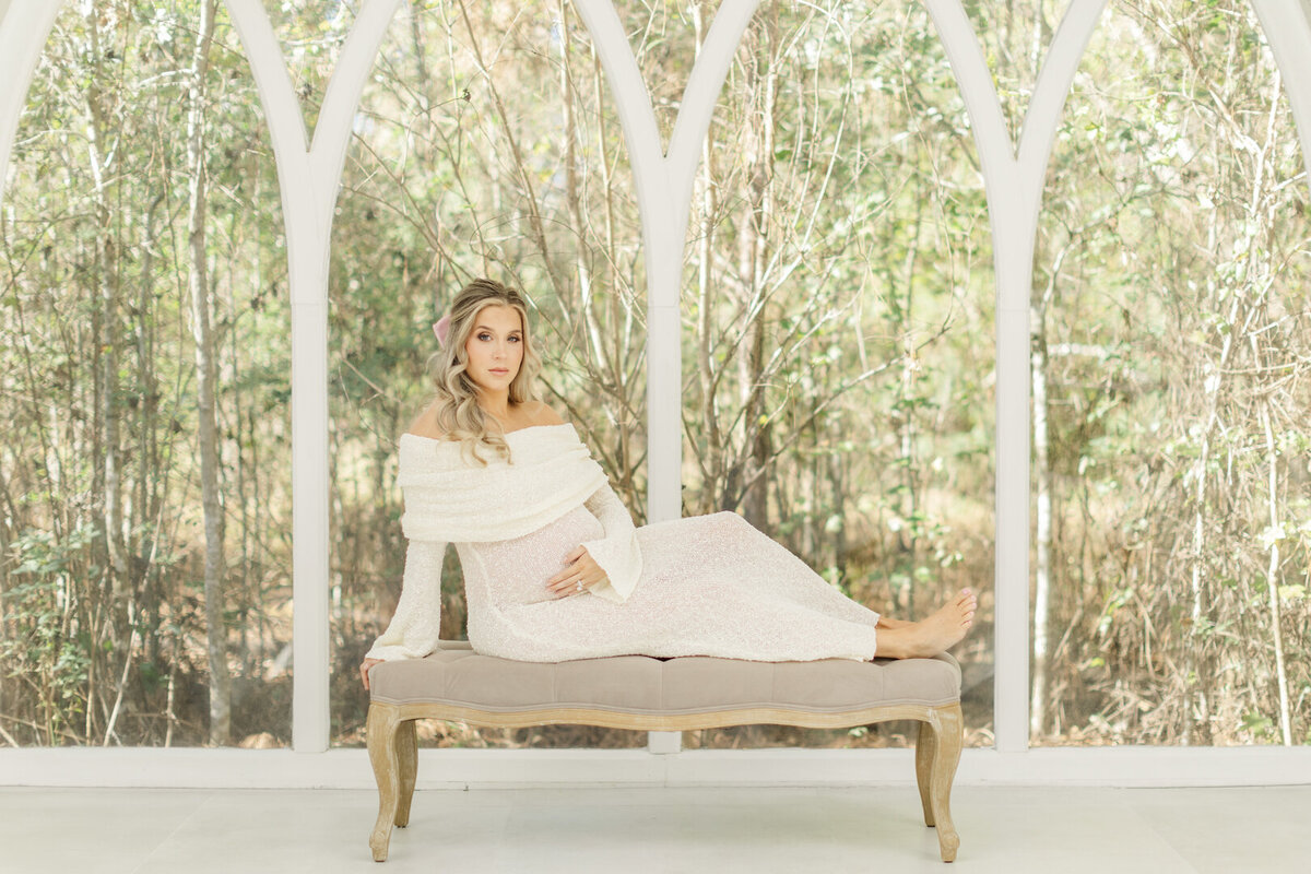pregnant mother seated on bench holding belly at the oat atelier for houston maternity photographer allie nichols photography