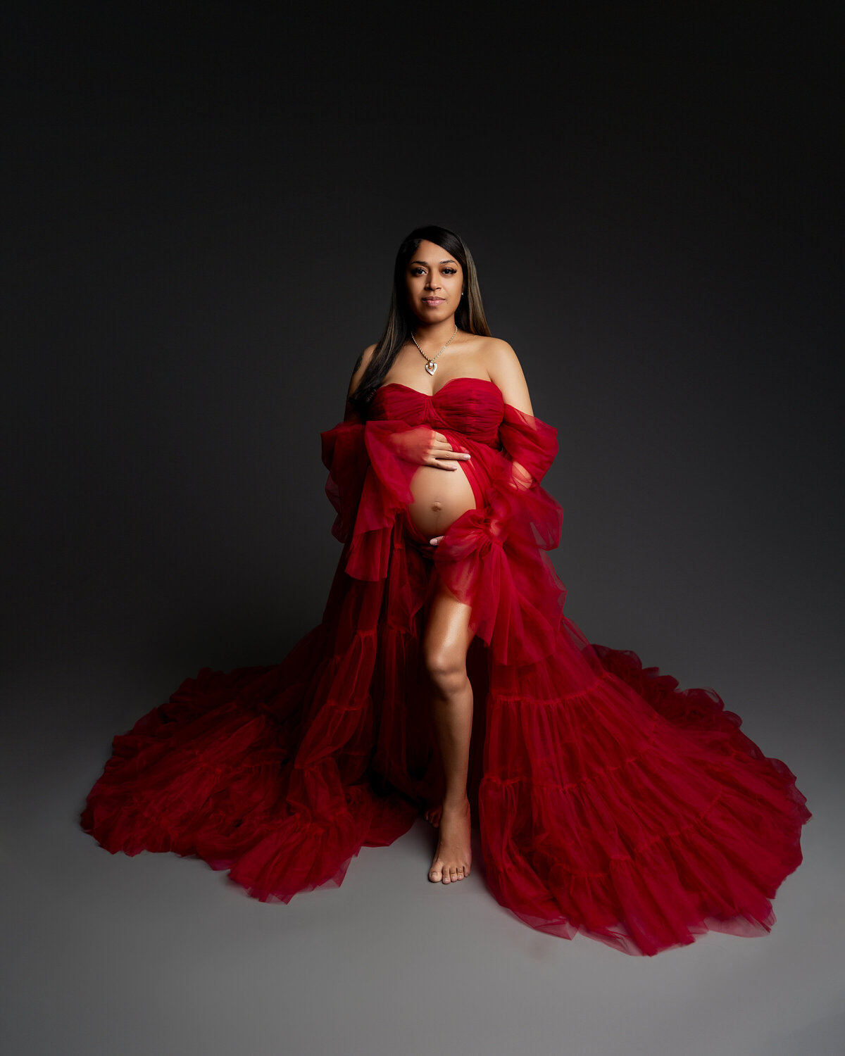 The expectant mother in a red dress gently holds her belly, radiating love and anticipation for the arrival of her baby. Captured by Inland Empire maternity photographer Kaitlyn Dawn Photography.