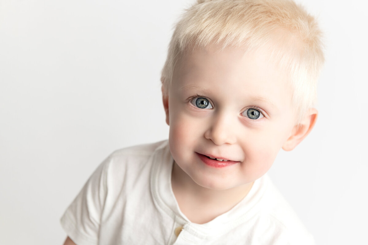 Personality portrait of a smiling toddler boy in white shirt—captured with playful warmth in studio light.