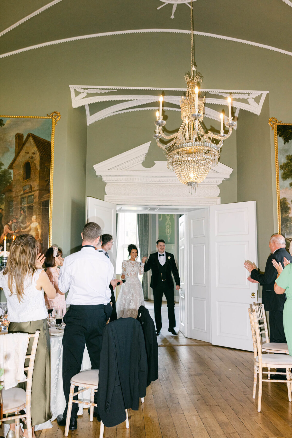 A wedding photo of the bride and groom walking into the reception hall with guests standing and celebrating at Luttrellstown Castle