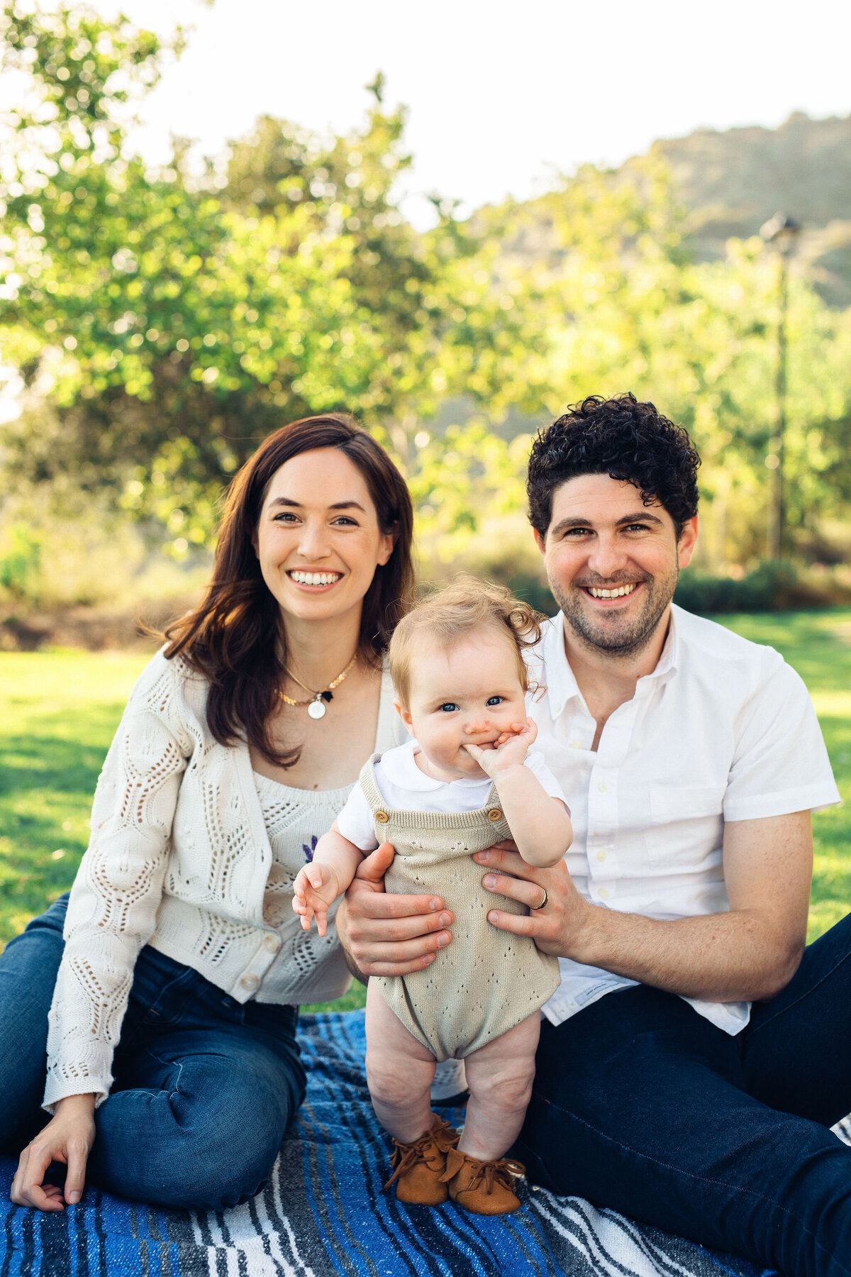 Family Portrait Photo Of Couple Holding Their Baby While Sitting On a Blue Fabric On The Ground Los Angeles