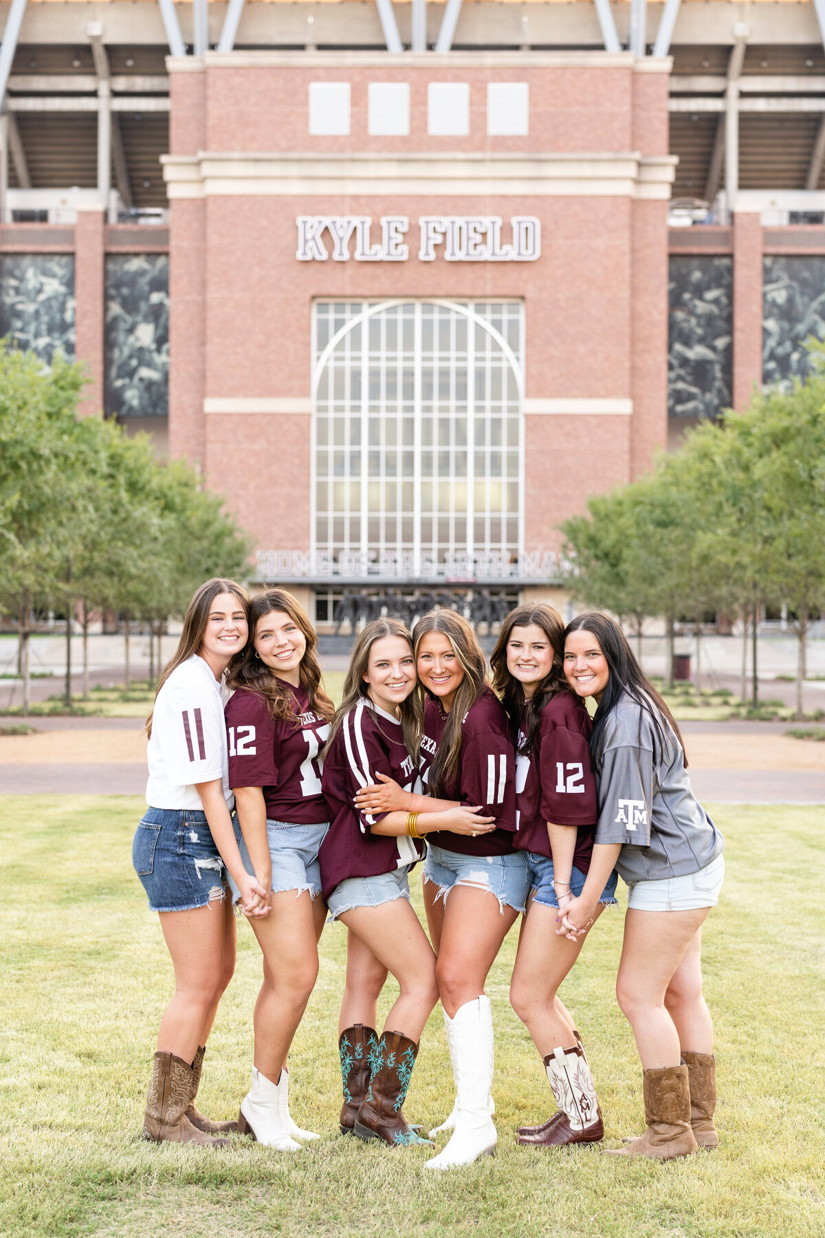 Texas A&M senior girls hugging while wearing A&M jerseys in front of Kyle Field at Aggie Park