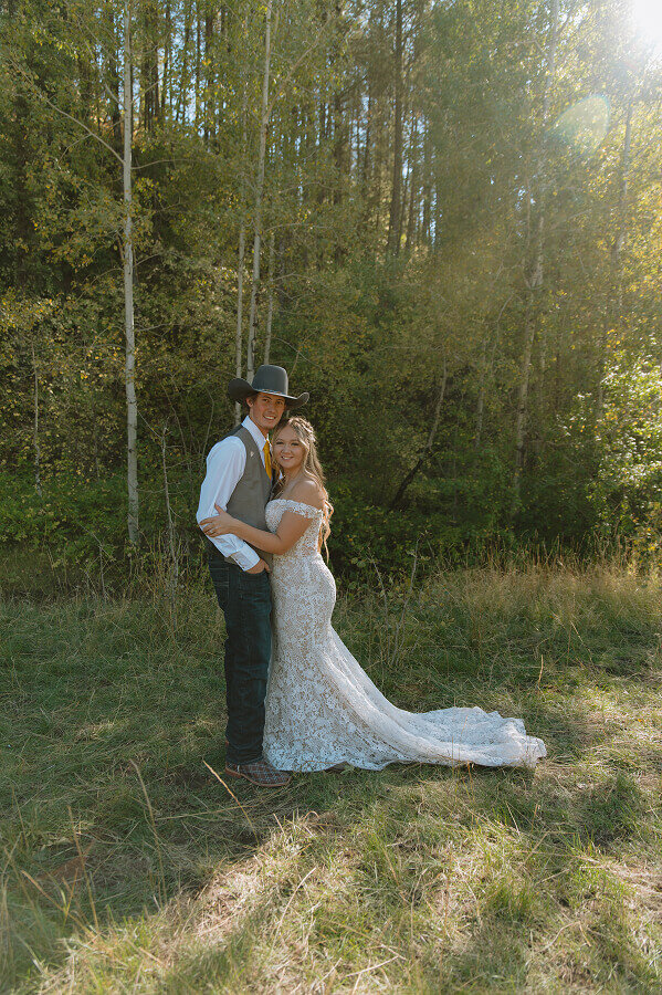 Facing each other, a bride holds the arms of her new husband. Both smile at the camera.