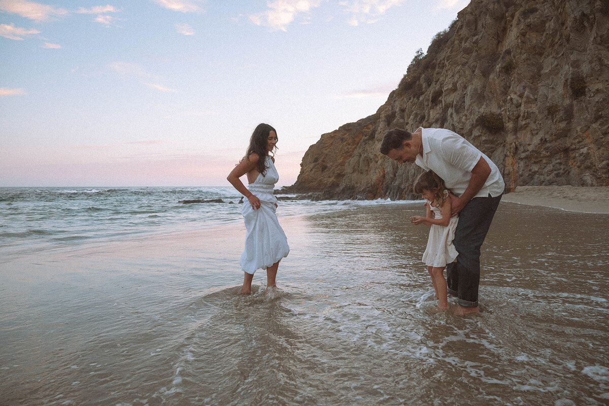 Orange County family enjoying playful candid moments at Laguna Beach during sunset with waves and cliffs in the background.