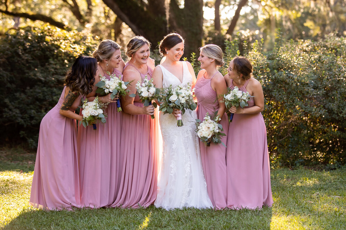 photograph of bridesmaids wearing mauve long dresses with the bride wearing white standing in front of oak trees at Eden Gardens State park, Florida 