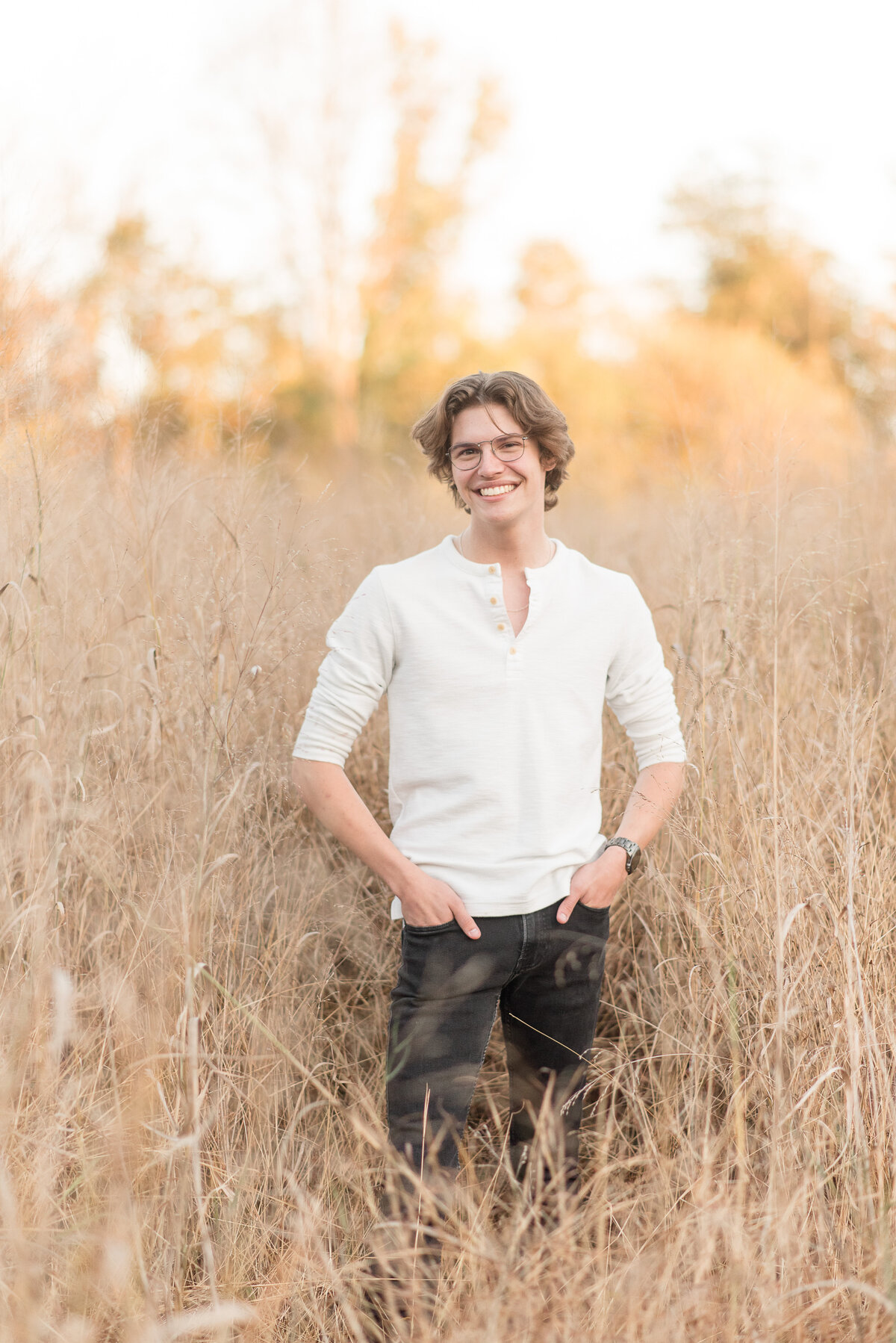 Senior guy standing in field of tall dry grasses with both hands in his pockets and smiling at camera at Lancaster County Park.