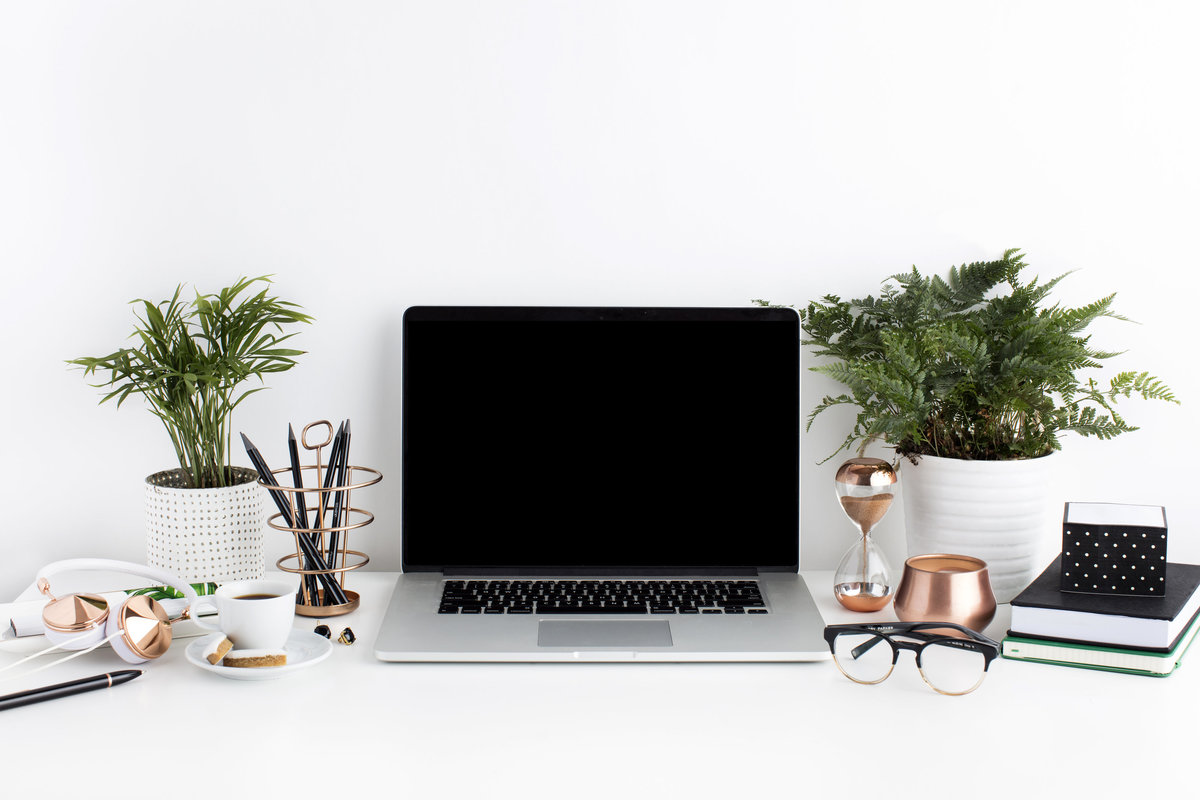 Image o a feminine working space, in tones of gold and blush. Roses sit in a mason jar next to an open laptop, and a inspirational text poster rests on the desk ledge. 