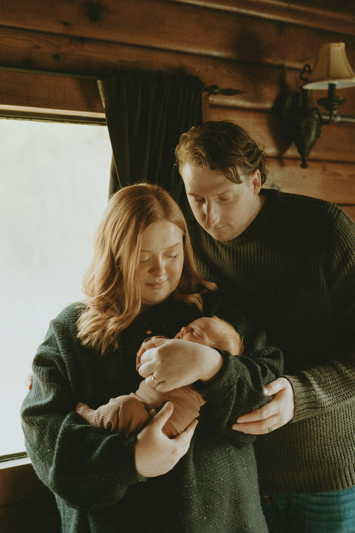 newborn lifestyle photo of a dad, mom, and baby snuggling in a cabin