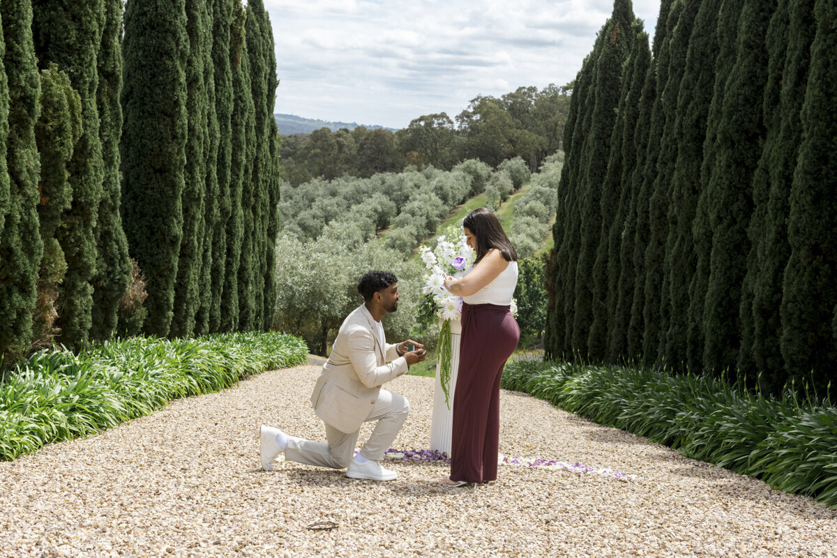 Bride and Groom standing on a mountain top. The wind is blowing in her hair and they are looking out to the view while hugging each other. The bride is a long sleeved wedding gown.
