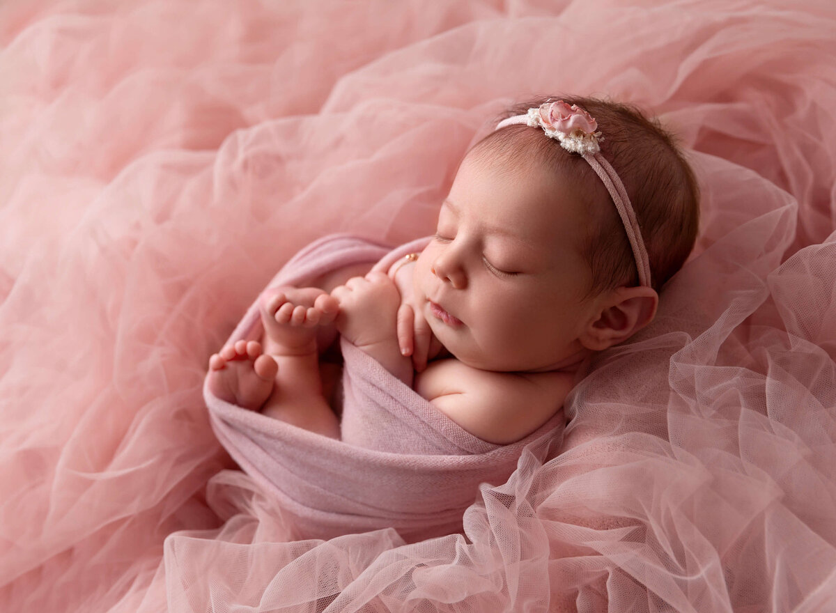 Newborn baby girl wrapped in pink with a pink flower headband