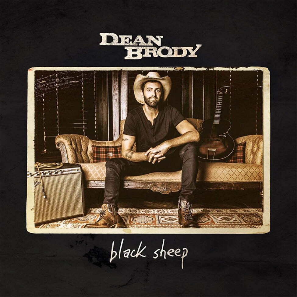 Nashville Country Music Single Cover Artist Dean Brody sitting on vintage sofa guitar beside him and amplifier on floor next to him wearing cowboy hat and cowboy boots black tshirt and black jeans Title Black Sheep