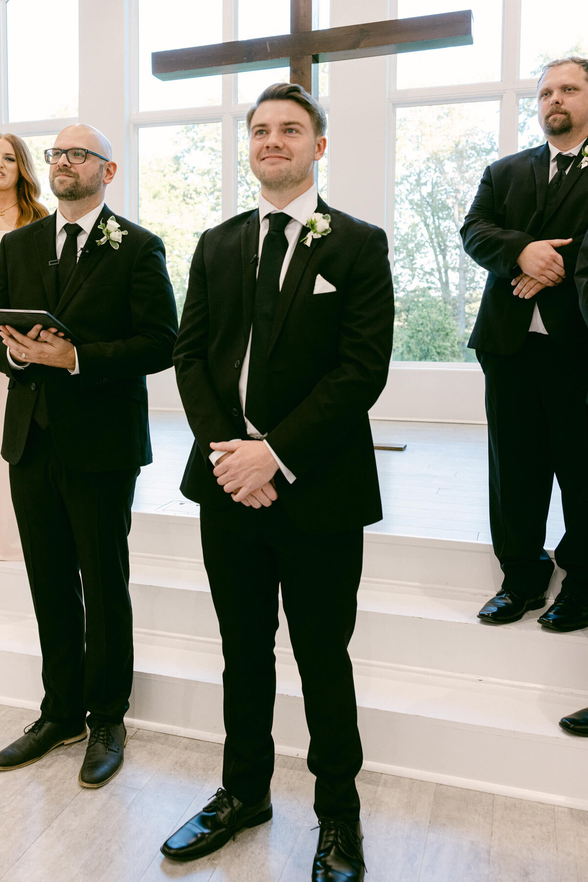 A wedding photo of a groom smiling seeing his bride walk down the aisle
