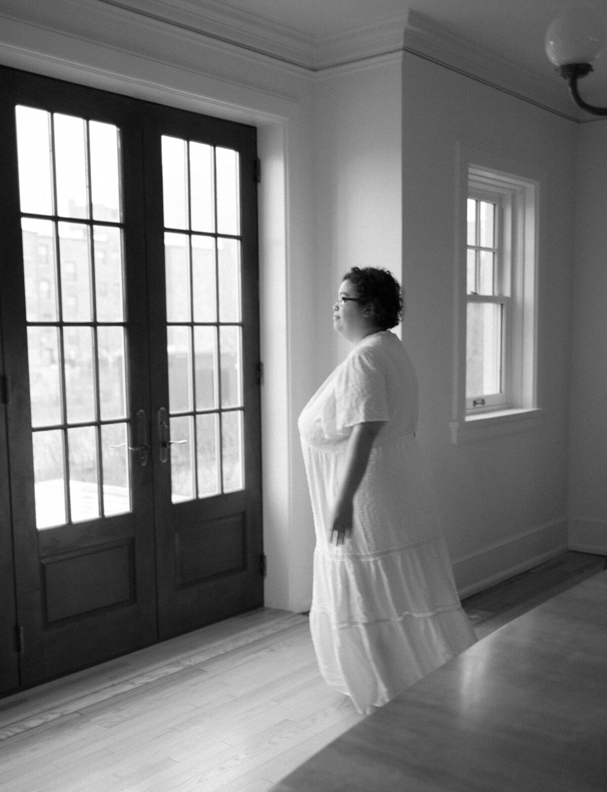 woman in long white cotton dress moves to historic dark wood windows, doors, ALEO Detroit