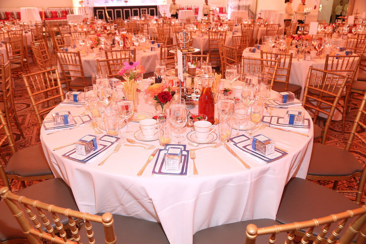 Round banquet table decorated with flowers, menus, and fine place settings.