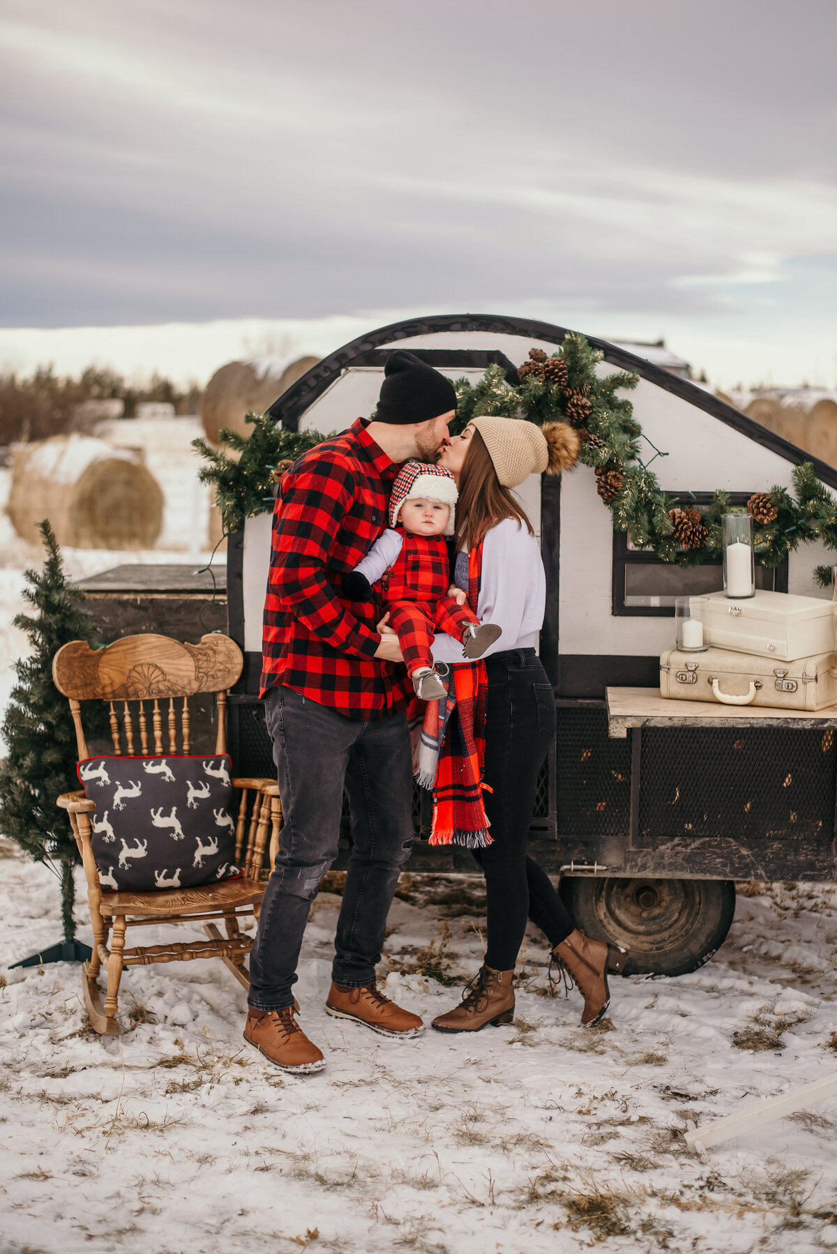 Man and woman kiss with infant in arms with a Christmas set up