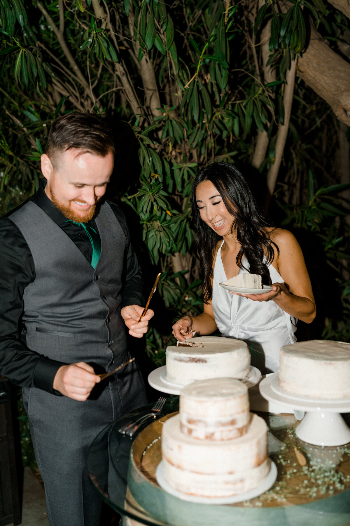 mride and groom cutting the white wedding cake while laughing together