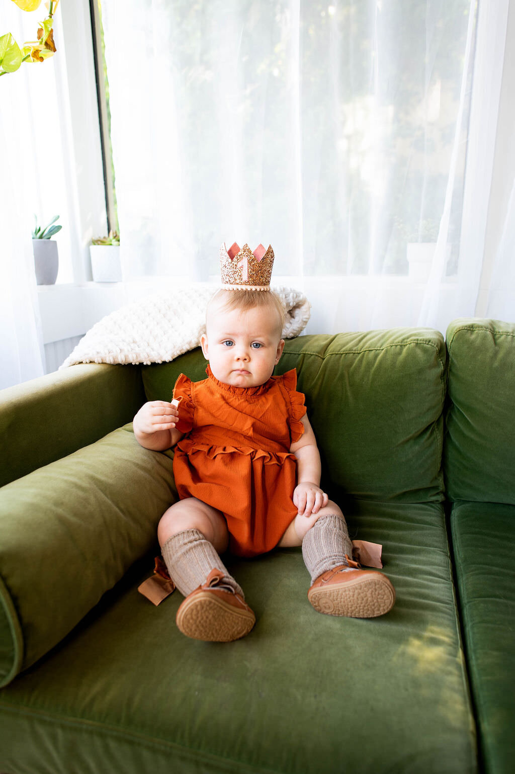 A baby with a "1" crown sitting on a couch.