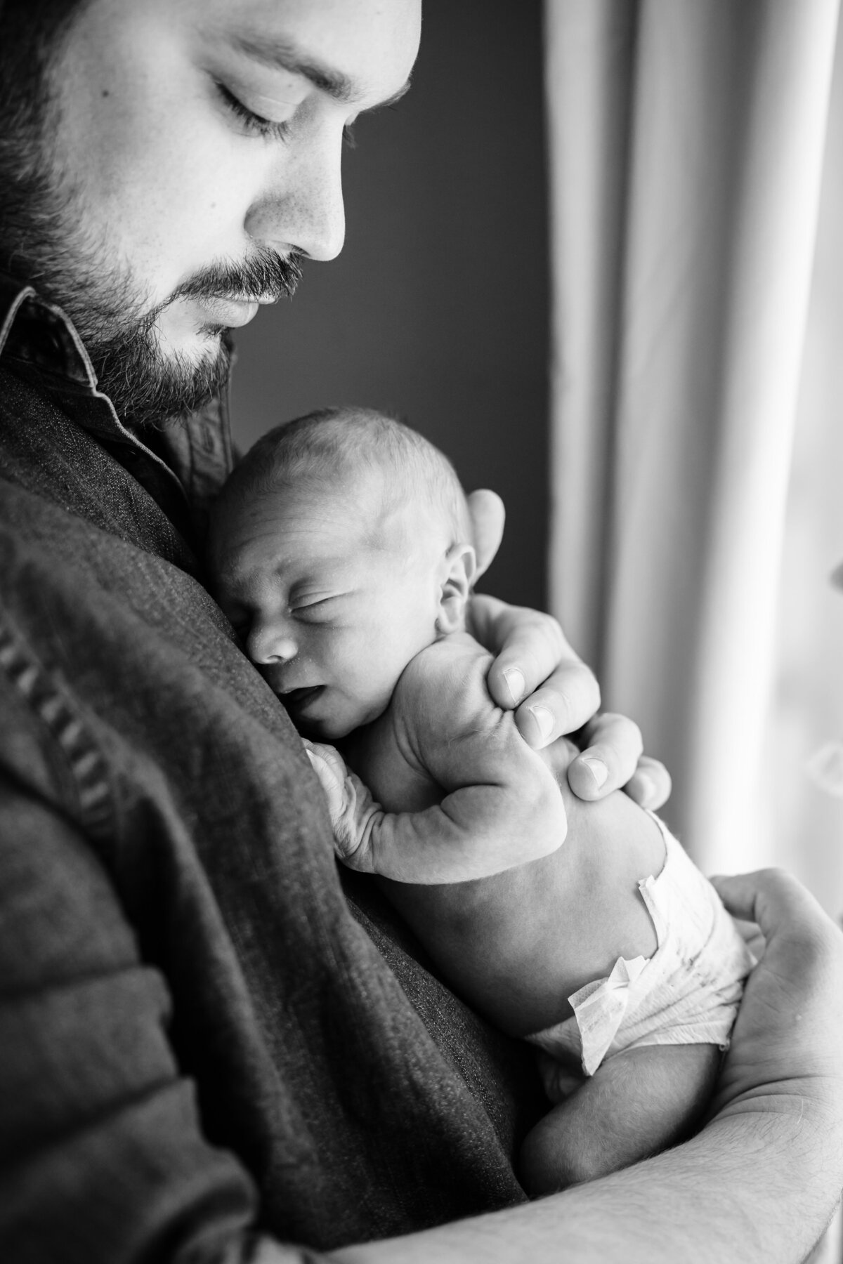 A black and white image of a father holding his newborn baby close to his chest.