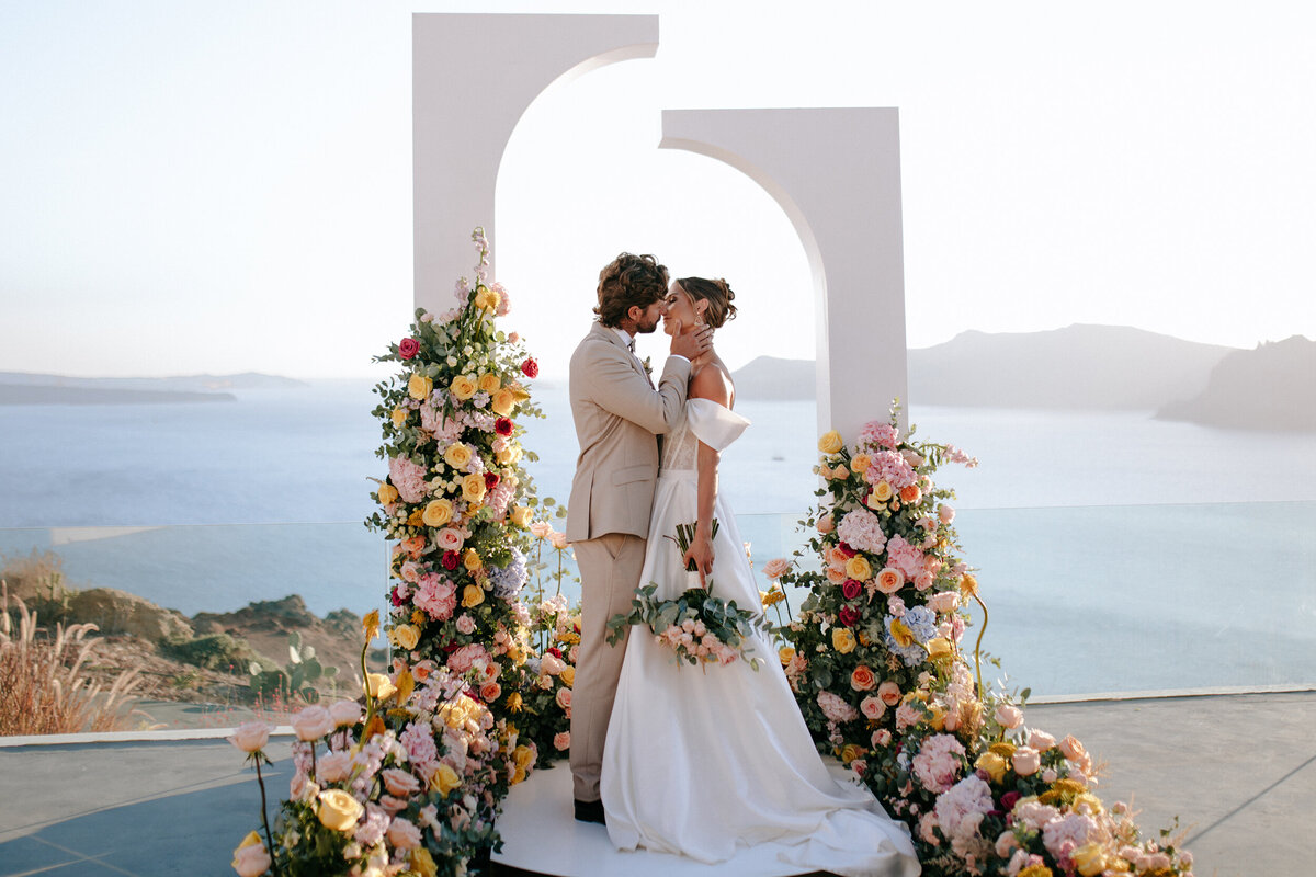 Bride and groom at colorful floral altar by the ocean at wedding ceremony