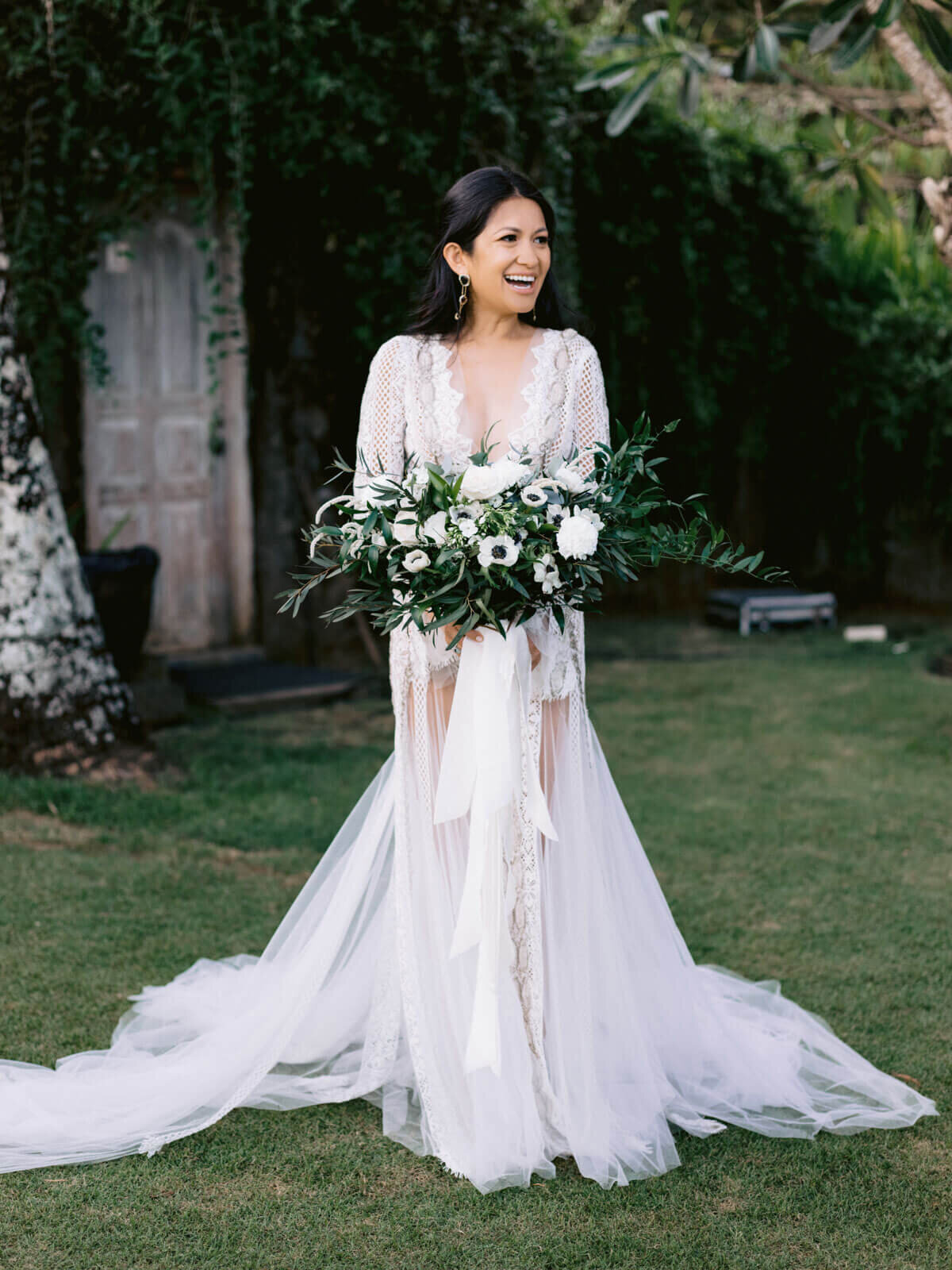 The gorgeous bride is smiling and holding her flower bouquet in Khayangan Estate, Bali, Indonesia. Image by Jenny Fu Studio