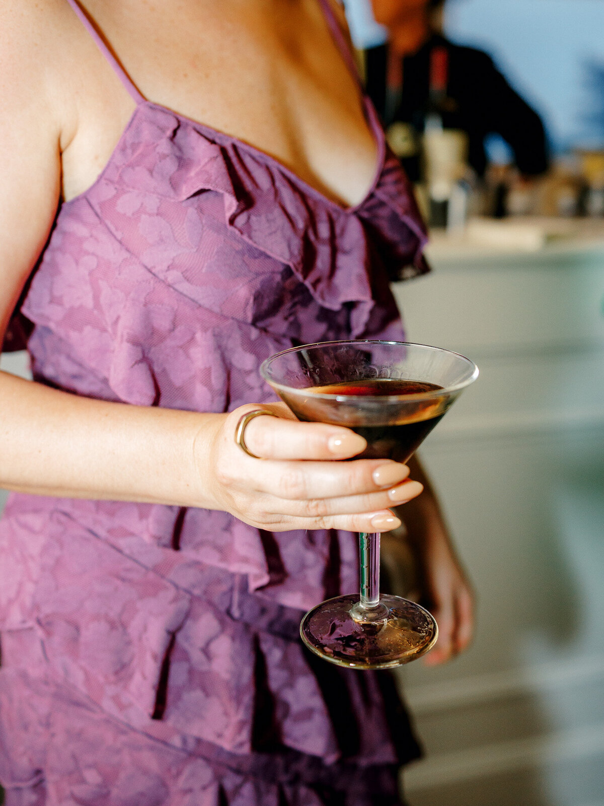Wedding guest in a purple dress holds an espresso martini