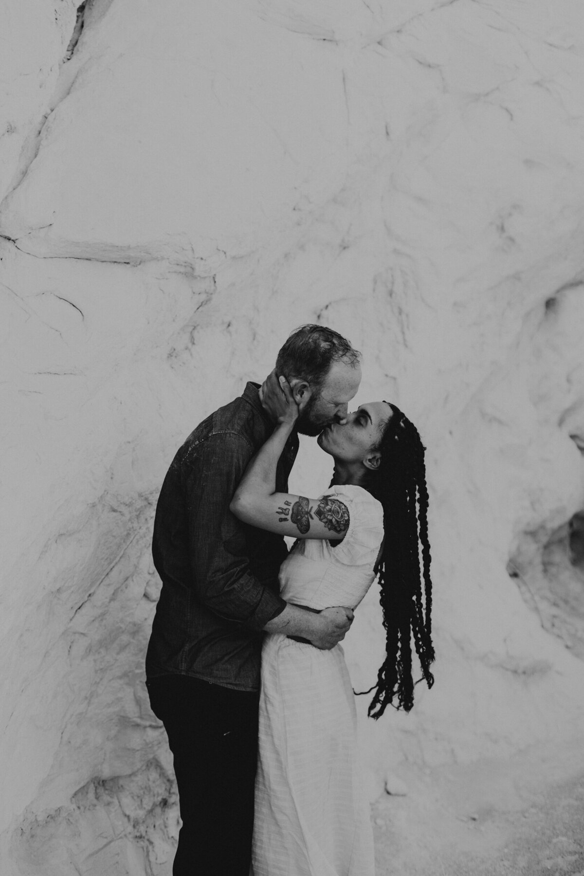 black and white photo of a couple kissing against a white rock