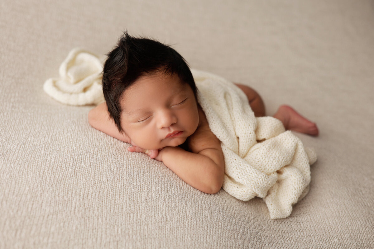 baby boy with dark hair sleeping on a cream blanket