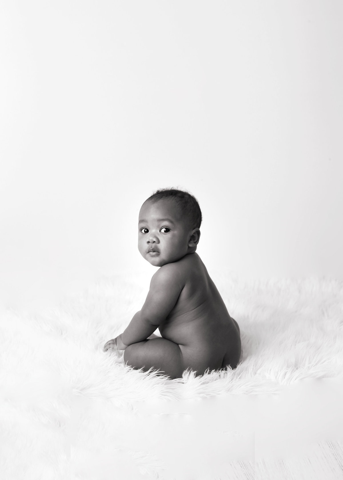 black and white image of baby boy on white fur rug