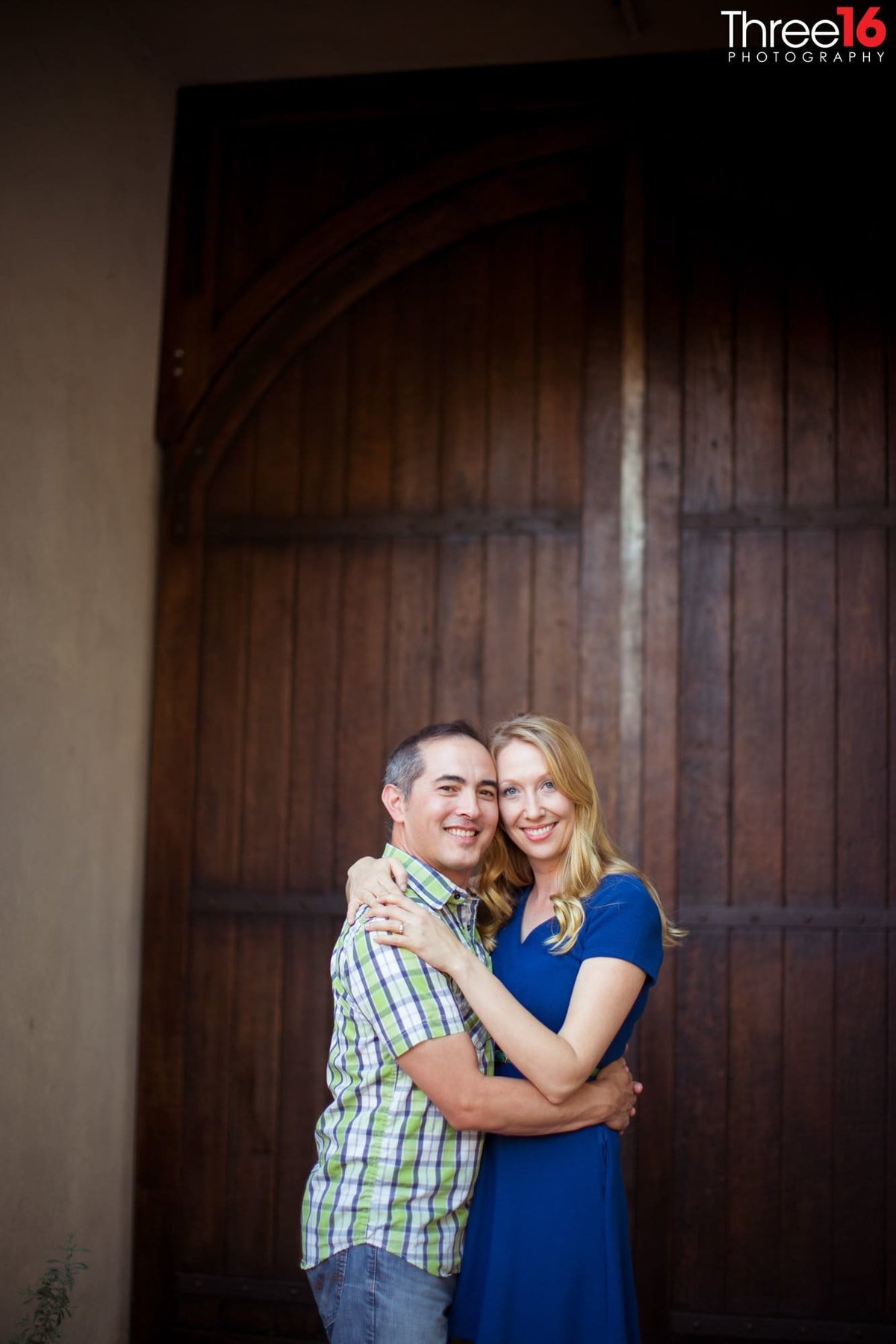 Engaged couple embrace each other in front of large wooden door at the Villa Del Sol