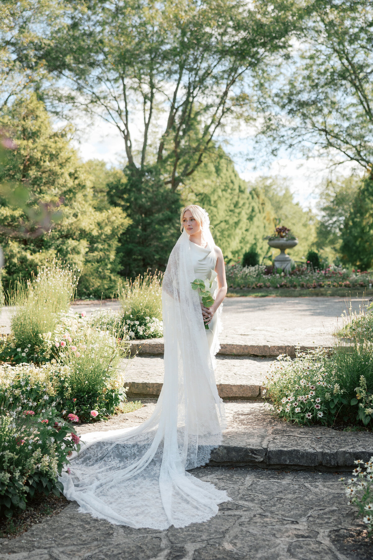 Bride stands solo in Dayton garden with lace veil, captured by wedding photographer from Philadelphia.