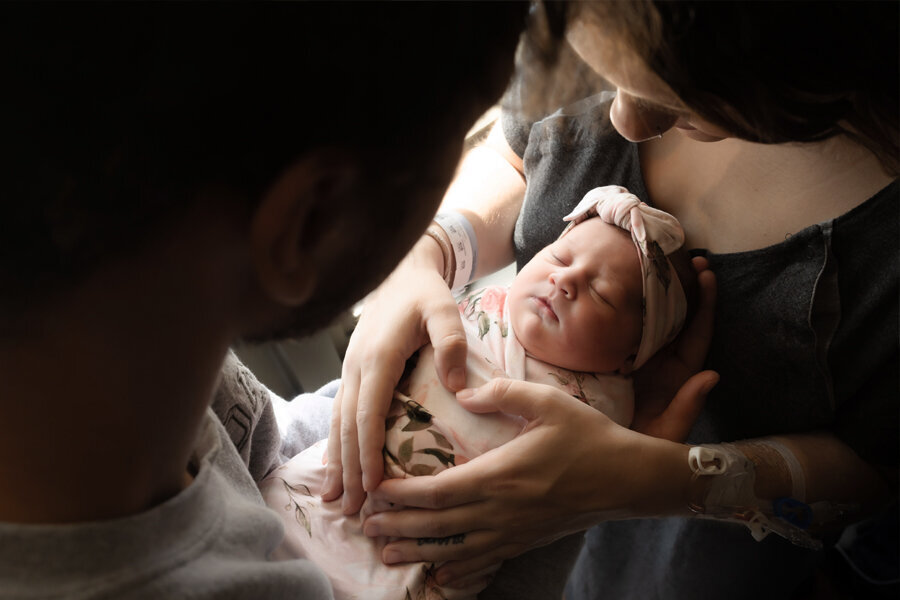 Newborn baby held between parents with mom's hands on baby's chest.