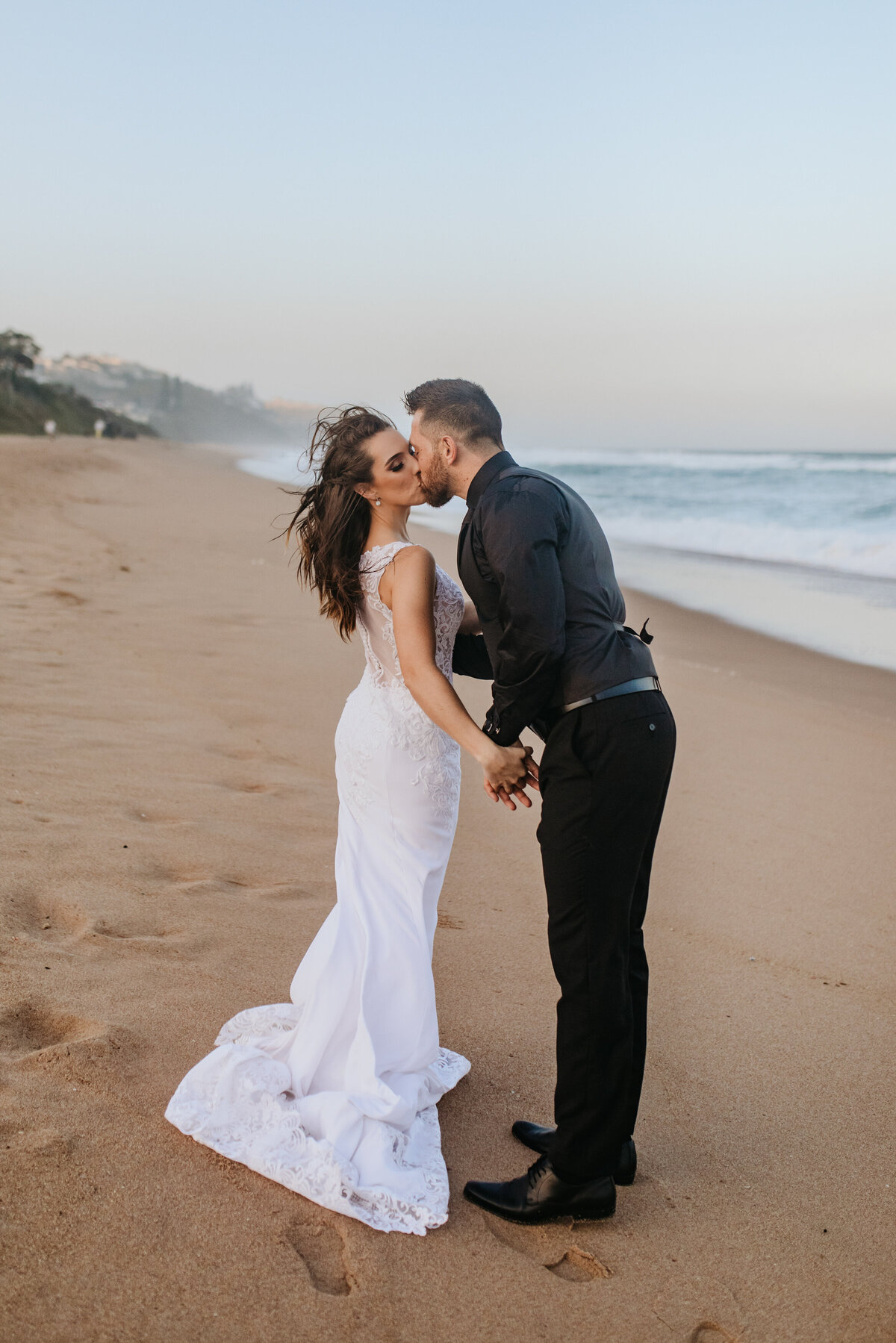 Bridal couple share a windy kiss on the beach. 