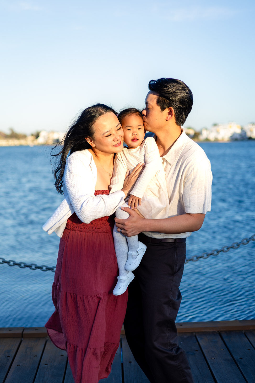 Parents cuddling daughter by the water under evening light in San Mateo – Bay Area Family Portfolio – Ellobelle Photography
