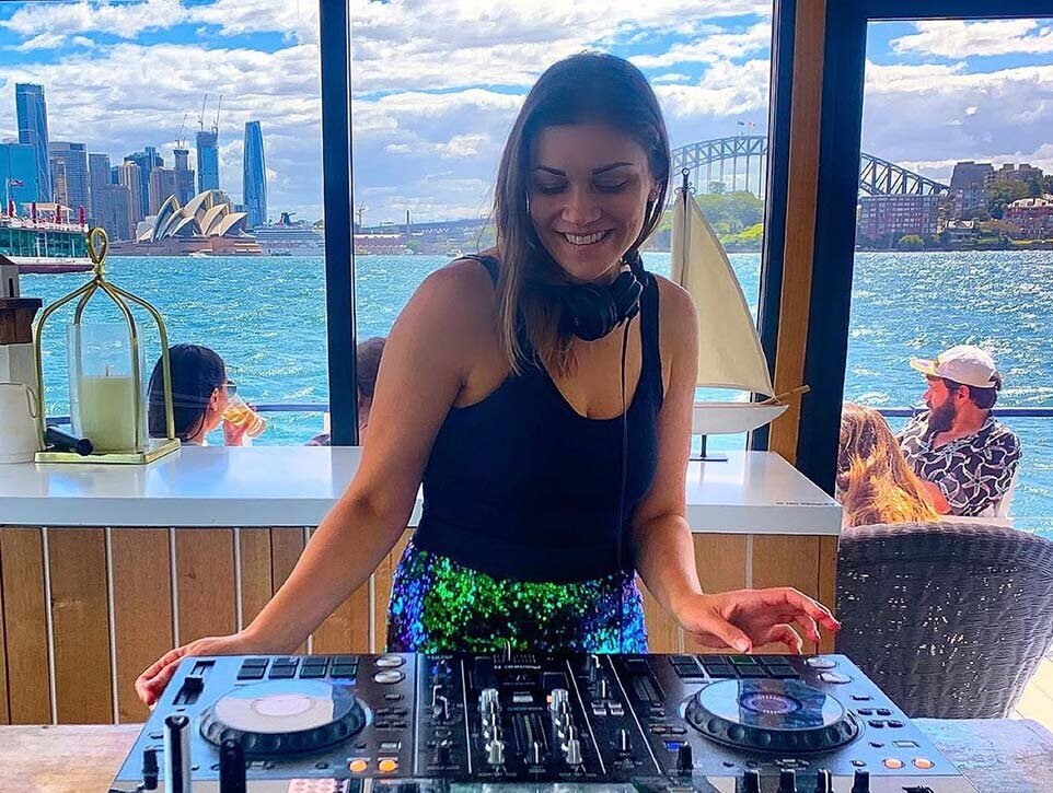 Female DJ performing on a boat with Sydney Harbour and the Opera House in the background.