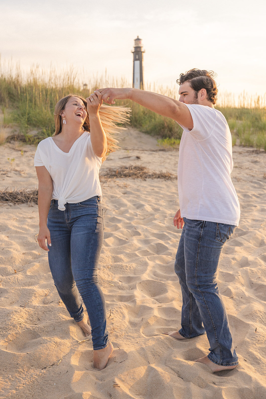 Couple twirls on a beach with the cape henry lighthouse in the background