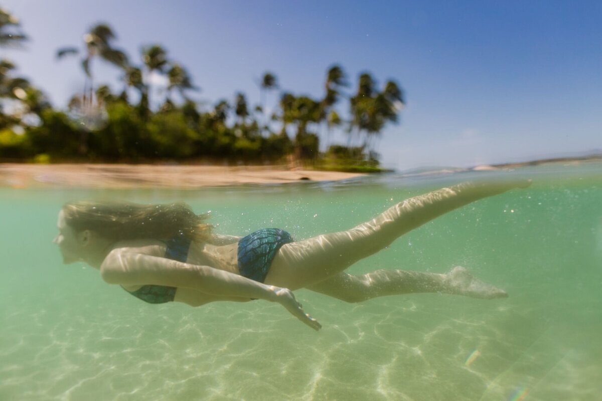 A young girl swims underneath the water with palms showing in the background.
