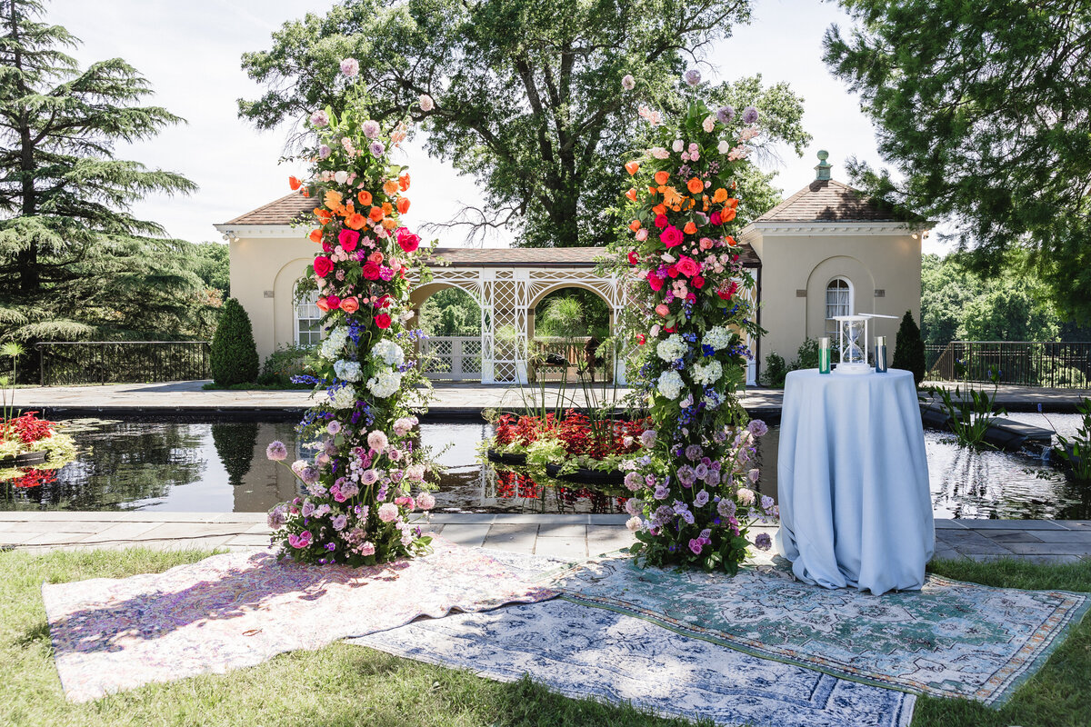 Vibrant floral arch with pink,  orange, blue and purple flowers at an outdoor  ceremony at the Belmont Manor House.